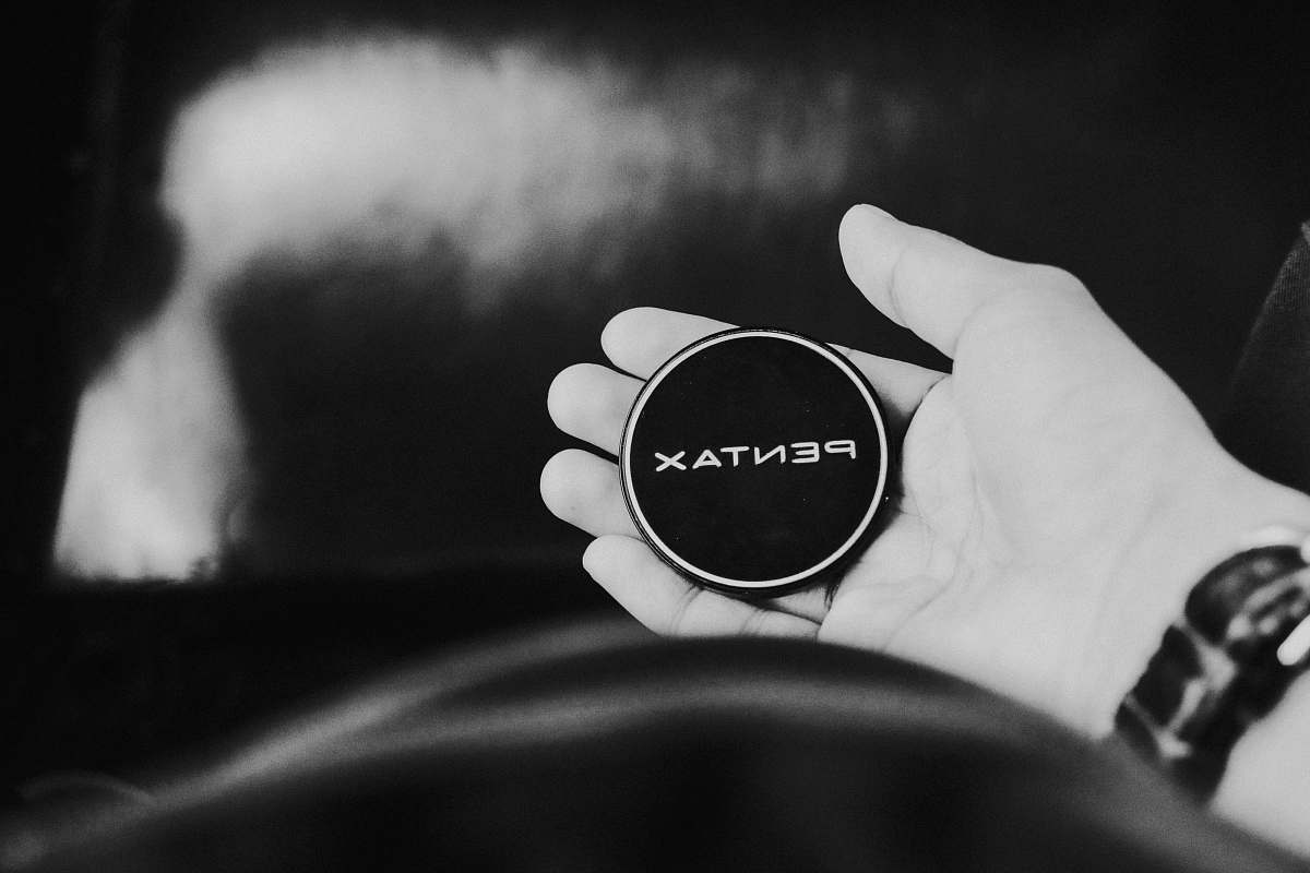lens cap grayscaled photo of person's leeft hand pentax